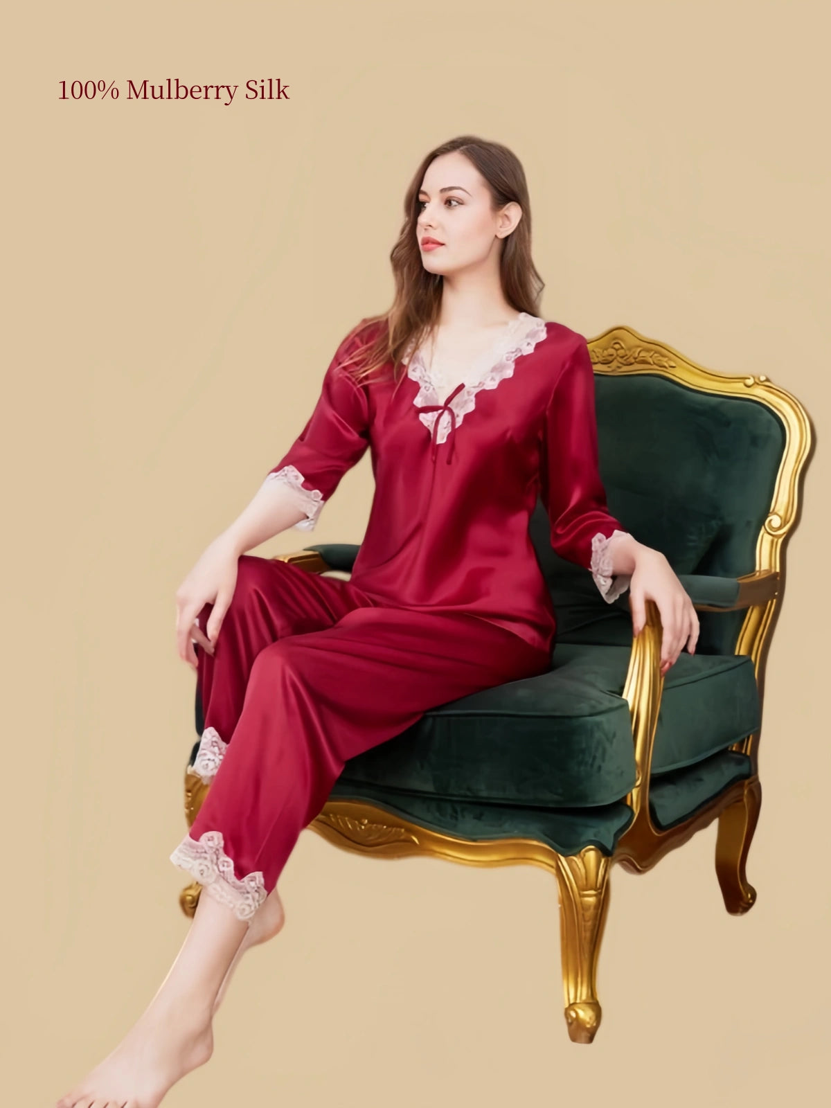 Model seated in Silkgala Jujube Red silk pajamas with lace-trimmed V-neck, decorative bow, floral lace sleeve cuffs and matching pants.