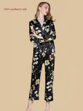 Full front view of Silkgala black floral silk pajamas featuring a button-front shirt, chest pocket, contrast piping and relaxed long pants.