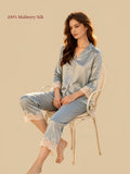 Model seated in Silkgala Green mulberry silk pajamas featuring three-quarter sleeves, delicate floral lace detailing and matching straight-leg pants.