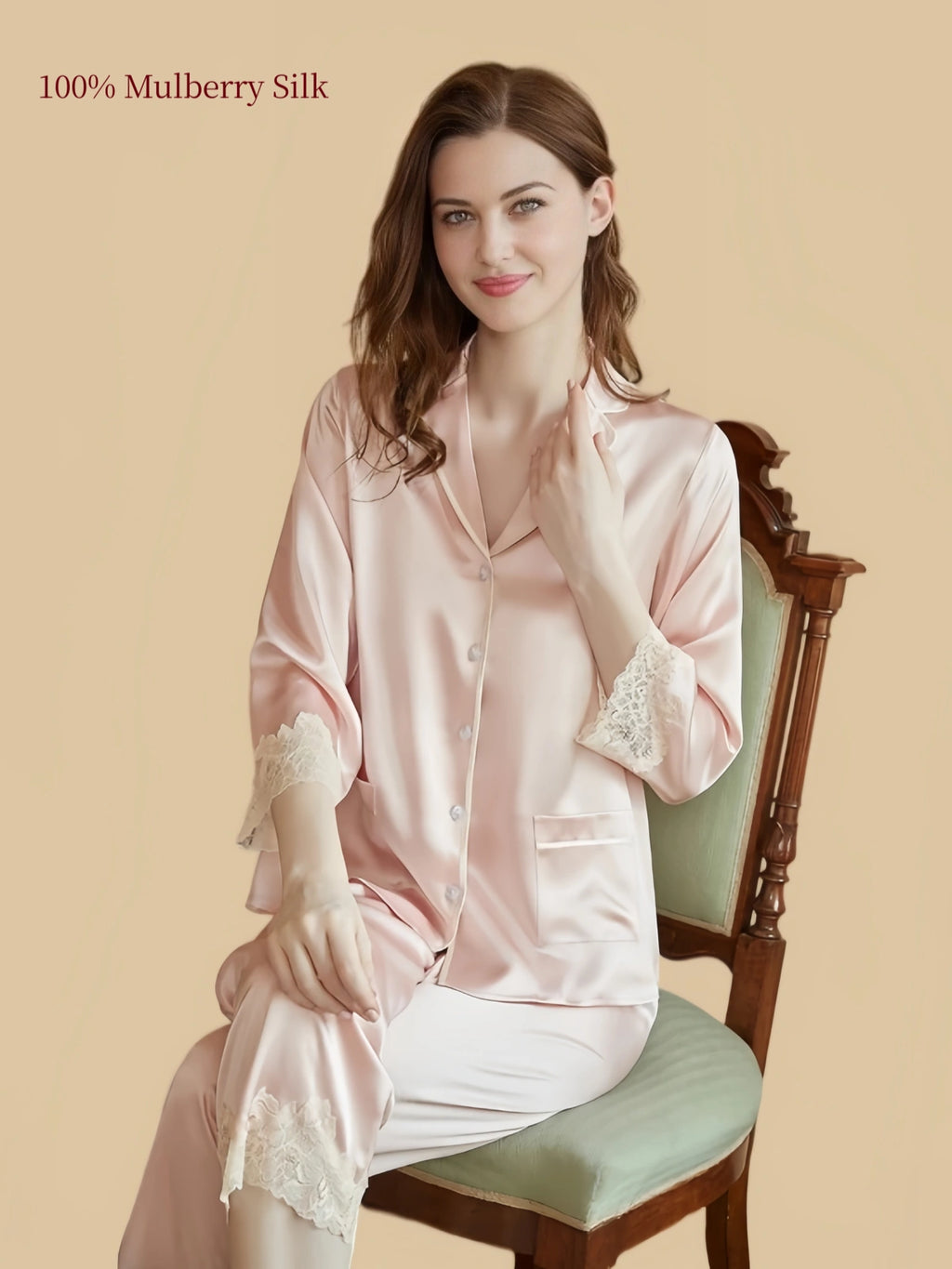 Model seated wearing Silkgala Pink silk loungewear two-piece with a notched collar, front buttons, floral lace cuffs and matching pants.