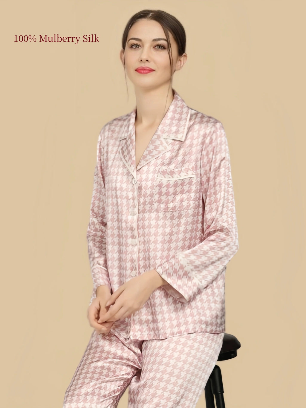 Seated model wearing Silkgala Pink Houndstooth silk pajama set with a notched collar, chest pocket and long straight-leg pants.