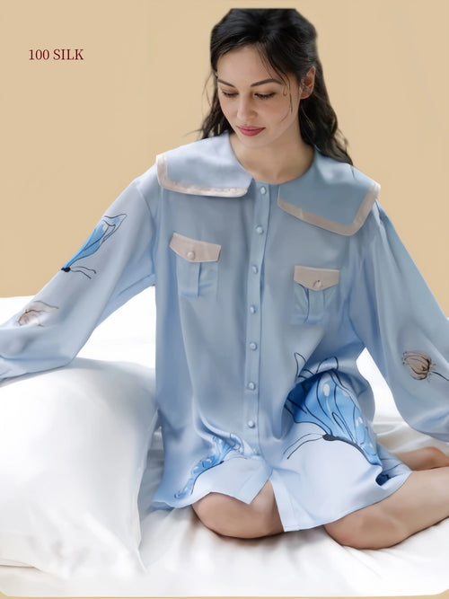 Woman seated in a Dusty Blue 19 momme mulberry silk sleep dress with butterfly floral print and sailor collar
