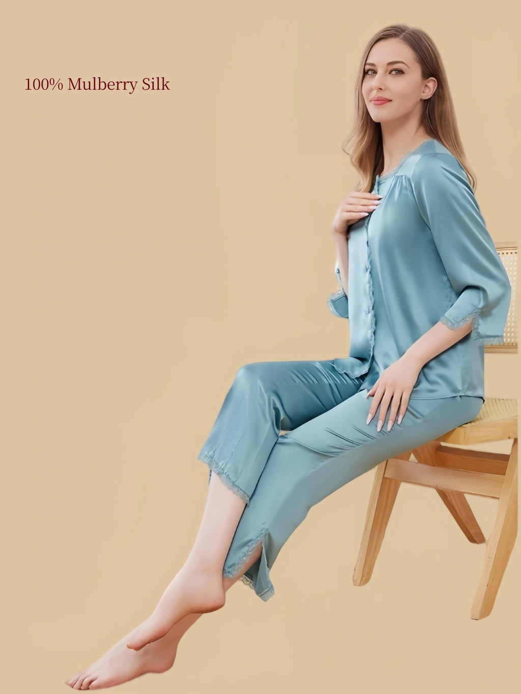 Model seated in Peacock Green Silkgala silk pajamas, showing the softly gathered square neckline, button-front top and lace-trimmed pant hems.